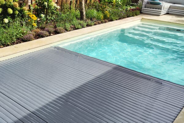 Motorisierte Unterflur-Poolabdeckung, die sich schützend über die Wasseroberfläche eines GFK-Beckens schiebt.