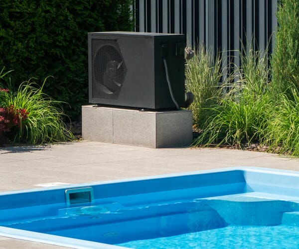 Moderne Luft-Wasser-Wärmepumpe zur Poolbeheizung, installiert neben einem eingelassenen Schwimmbecken im Garten.