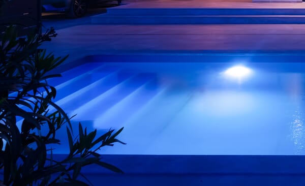 Schwimmbecken bei Nacht mit eingeschalteten, smarten Unterwasserscheinwerfern.